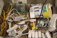 Photo showing a variety of electrical components including power cords, yellow connectors, white light switches, and metal electrical boxes inside a box.