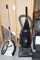 Front view of Bissell PowerForce upright vacuum and Conair garment steamer side by side on floor.