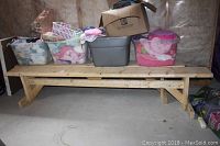 Wide shot of one unfinished wooden bench with storage bins and boxes placed on top in storage area.