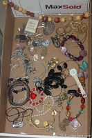 Top view of various mixed costume jewelry pieces including beaded bracelets, metal chains, clip-on earrings and brooches laid out in a box.
