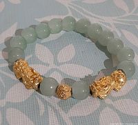 Full view of jade bead bracelet showing two gold-plated Pixiu charms and center gold bead