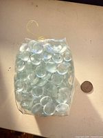 Front view of sealed bag filled with clear glass flat pebbles beside coin for size reference