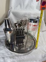 All items grouped: stainless steel shaker, glass recipe shaker with lid, round tray, bar tool stand with five cups and strainer