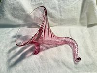 Side view of pink glass cornucopia vase showing flared mouth, ribbed body, curled tail and support foot
