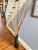 Full view of teal glass vase with sticks in hallway