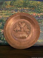 Front of copper plate showing embossed flower basket design and decorative rim