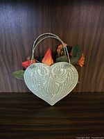 Front view of embossed heart-shaped metal wall planter with faux flowers