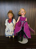 Both dolls side-by-side on shelf showing size, outfits, stand