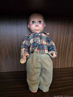 Front view of 14-inch baby doll in plaid shirt and green pants