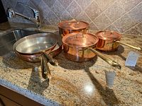 Overview of four copper pans and three lids on countertop