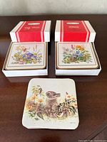 Two boxed coaster sets in red striped boxes and one loose stack of wildlife-print coasters displayed on tabletop
