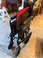 Side view of folded black EZee Life transport wheelchair showing red-trimmed backrest and front casters