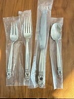 Four flatware pieces in plastic sleeves on wood surface