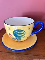 Large yellow and blue ceramic cup planter on saucer, rooster motif visible