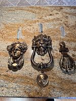 Three antique brass finish decorative door knockers with hardware displayed on countertop