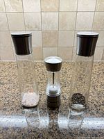 Front view of all three stainless and glass grinders showing relative sizes and residual contents