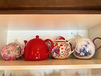 Shelf view of four ceramic/porcelain teapots with lids displaying patterns and colors