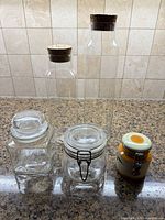 Group shot of two tall bottles, two glass jars, one ceramic jar