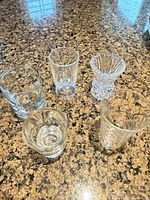 Five small clear glass vessels on countertop showing shapes and condition