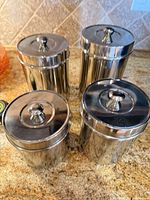 Four polished metal canisters with lids displayed on countertop
