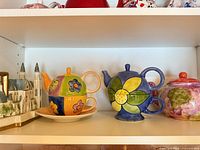 Shelf view showing multicolor patchwork tea-for-one set on saucer next to blue flower tea-for-one set