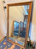 Full view of rectangular gilt wood wall mirror leaning against wall