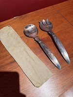 Serving spoon, fork, and cloth sleeve on wood surface