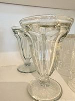 Two clear pressed glass pedestal dessert glasses side view