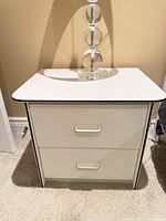 Front view of one white two-drawer nightstand showing drawer fronts, pulls and black trim