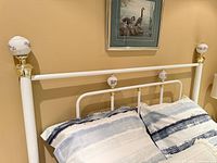 Headboard portion of white metal queen bed with porcelain floral finials