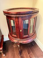 Front view of closed round mahogany display cabinet showing glass panels and carved details