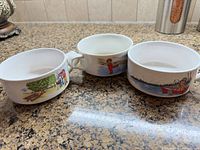 Three ceramic handled bowls showing exterior children’s illustrations
