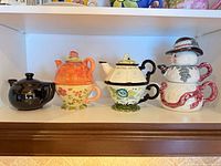 Front view of four distinct ceramic teapots lined on a shelf