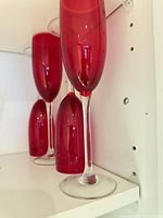 Side view of red glass champagne flutes on shelf