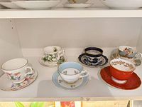 Six assorted teacups with matching saucers displayed on shelf