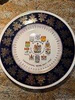 Front view showing cobalt rim, gold maple leaves, coats of arms and centennial text