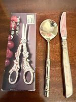 Box for silver-plated grape shears, spoon, butter knife on wooden surface