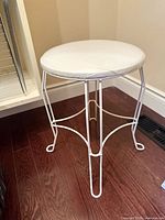 white metal vanity stool with padded seat on hardwood floor