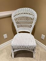 Front three-quarter view of white wicker chair showing decorative back and seat