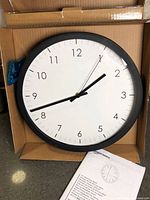 Clock in open box showing black frame, white dial, hands and numerals