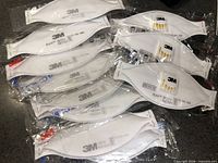 Group of eleven sealed 3M Aura respirators—eight unvalved, three valved—in individual pouches