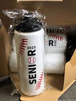 Open carton showing multiple white bottles with SENIOR 2025 baseball design