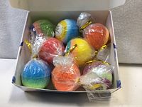 Open box showing eight colorful bath bombs wrapped in plastic
