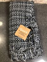 Folded black and grey woven blanket scarf with attached Just Cozy tag visible