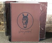 Front covers of three spiral-bound horse show journals, two still wrapped