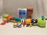 All items lined up showing variety of baby toys including caterpillar, teethers, bath toy tube and balls