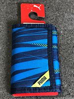 Front of folded wallet showing blue pattern and yellow Puma branding, hanger tab attached