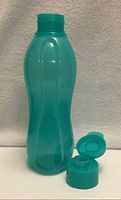 Full view of turquoise plastic drinking bottle with cap removed and placed in front