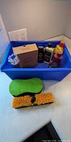 Overall view of tote showing cleaning chemicals, mouse traps, sponge and brush