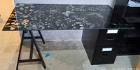 Full view of glass top desk supported by trestle leg and file cabinet